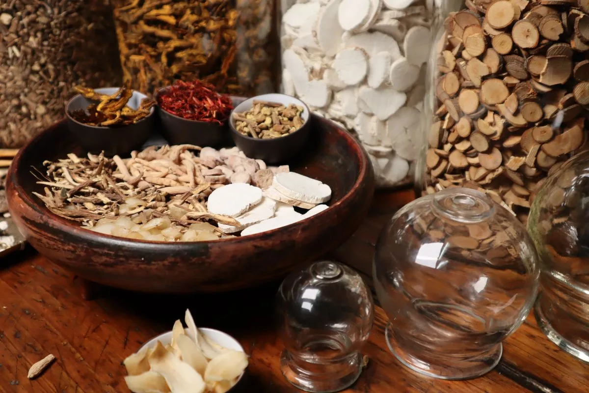 A wooden bowl of dried Chinese herbs and roots with small dishes of red saffron and glass jars