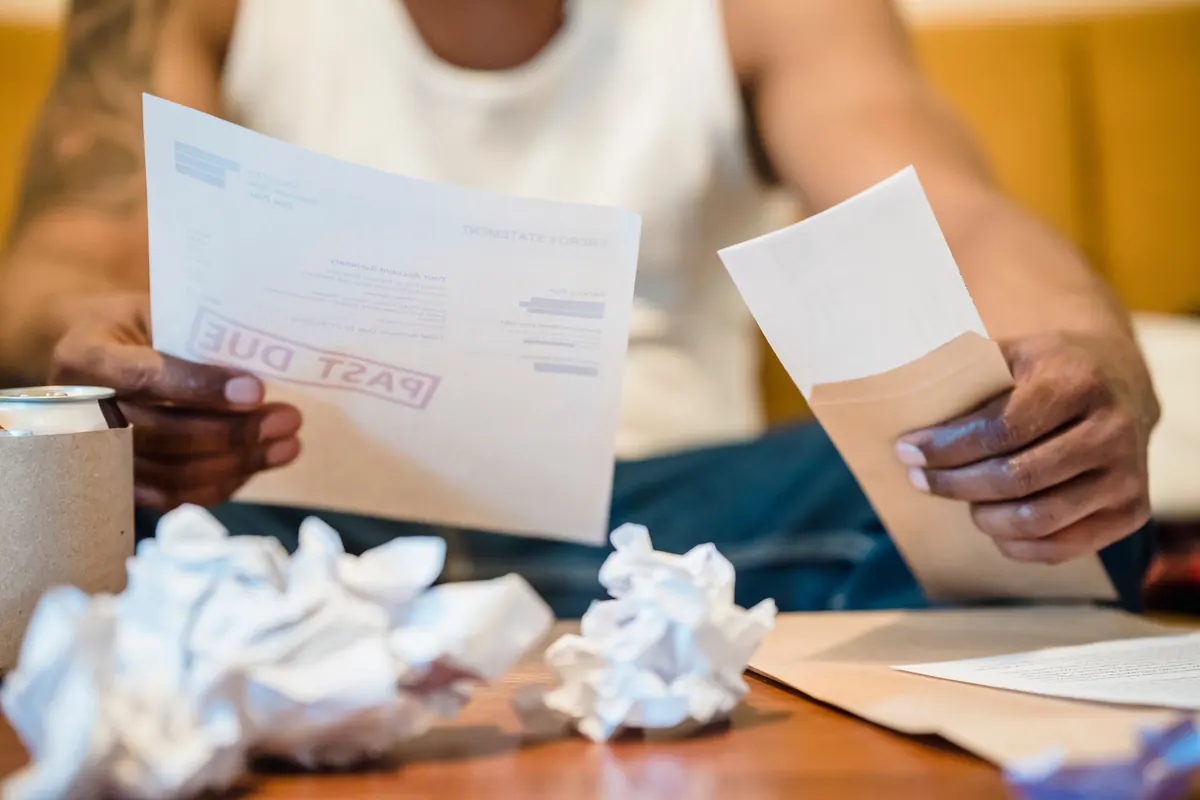 A man holding a letter stamped PAST DUE and an envelope, with crumpled paper on the table in front