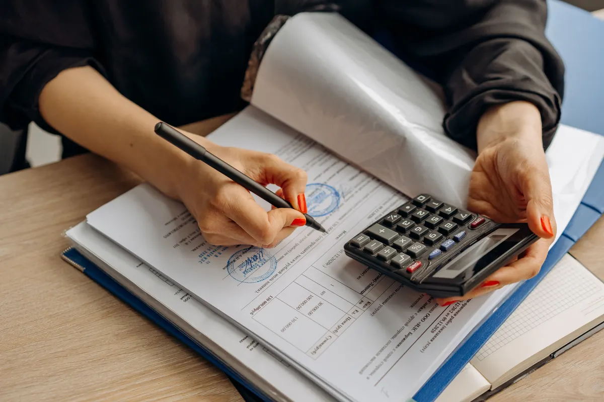 A woman with a pen and a calculator going over a stamped document in a blue binder