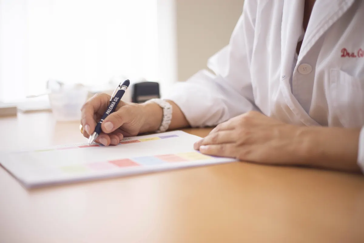 A doctor in a white coat writing with a pen on a color-coded chart at a wooden desk
