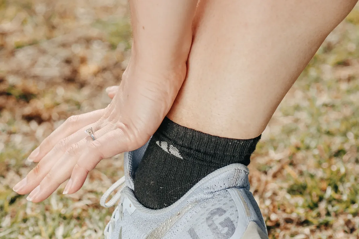 Close-up of a woman's hand touching her ankle just above a sneaker, on a grassy lawn